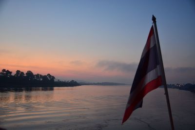 Red flag on lake against sky during sunset