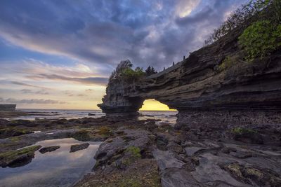 Rock formation on beach against sky during sunset