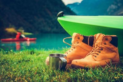 Close-up of shoes and mug with kayak at lakeshore