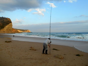 Man fishing on beach by sea against sky