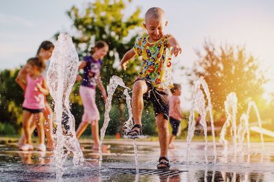 Full length of boy enjoying on fountain against sky