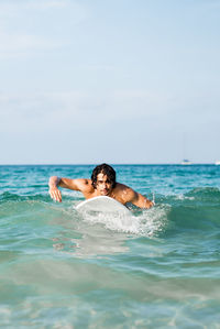 Full length of shirtless man in sea against sky