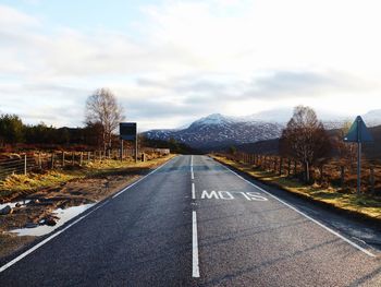 Empty road by trees against cloudy sky