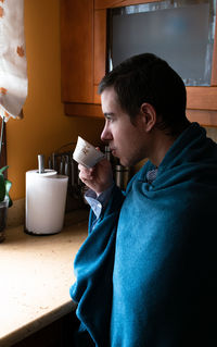 Side view of young man drinking glass at home