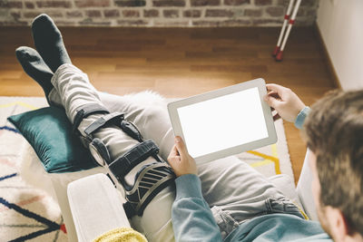 Injured man with knee brace using a tablet computer at home