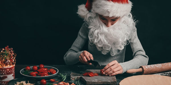 Caucasian teenage girl in a christmas hat with a beard cuts with a big black knife cherry tomatoes 