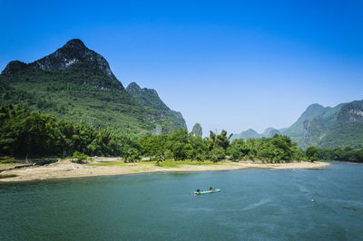 Scenic view of sea and mountains against clear blue sky