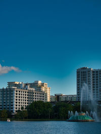 Buildings by sea against clear blue sky