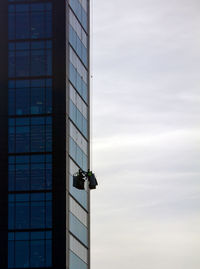 Low angle view of window washer against cloudy sky