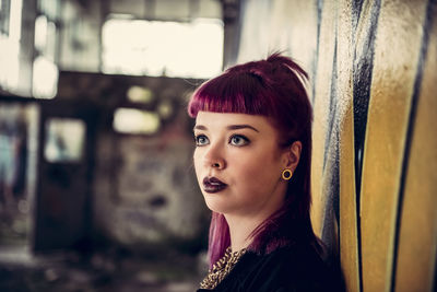 Young woman looking away standing against wall in abandoned building