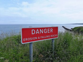 Warning sign by sea against sky