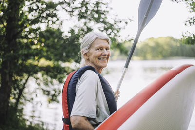 Portrait of happy senior woman holding paddleboard and oar