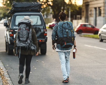 Back view of anonymous couple of backpackers walking along road towards car during adventure in australia