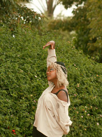 Young woman with arms raised standing against plants