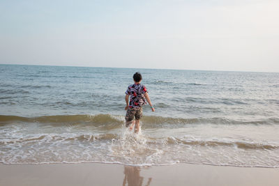 Full length of boy standing on beach against sky