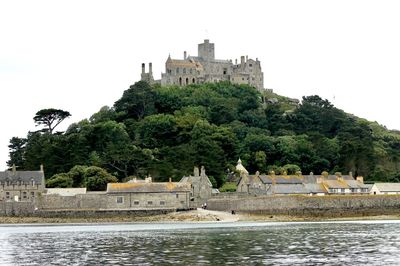 Castle on river by building against clear sky