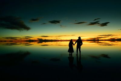 Silhouette couple standing at beach during sunset