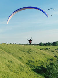 Person paragliding on field against sky