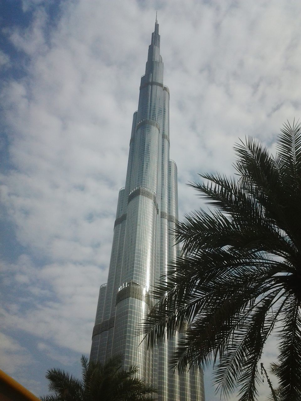 low angle view, architecture, built structure, building exterior, sky, tree, cloud - sky, tower, cloudy, tall - high, cloud, branch, growth, place of worship, religion, palm tree, outdoors, no people, day, dusk