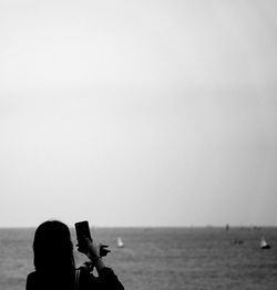 Man photographing at sea against clear sky