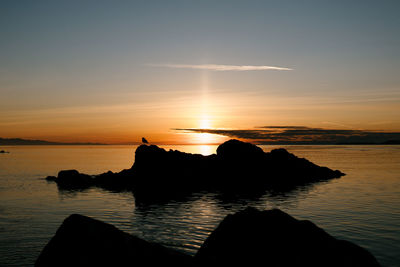 Silhouette rocks on sea against sky during sunset