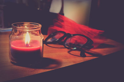 Lit candle in jar and eyeglasses on table