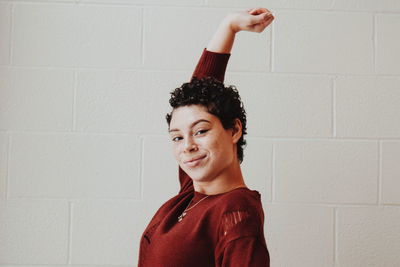 Portrait of smiling young woman standing against wall