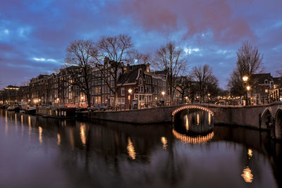 Illuminated bridge over river against sky in city