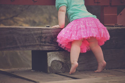 Low section of girl standing by wooden seat