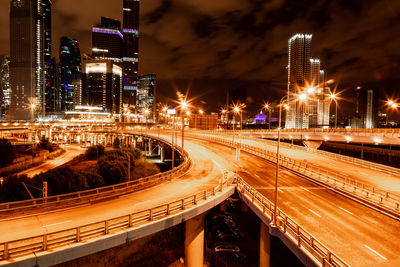 Light trails on road by illuminated buildings in city at night