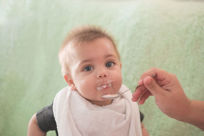 Hand feeding baby boy against wall at home