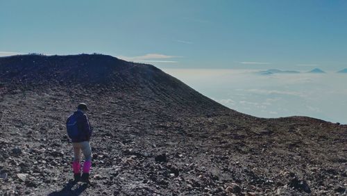 Rear view of man standing on mountain against sky