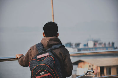 Rear view of man sitting on railing against sky