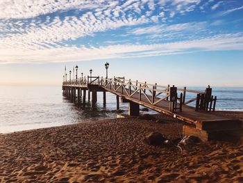 Pier on beach against sky during sunset