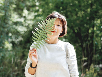 Young woman is hiding her eyes with fern leaf. symbol of life, tranquility and unity with nature. 