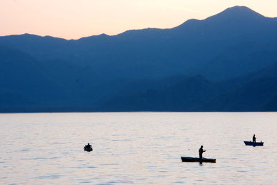 Three silhouetted fishermen, each in a small boat. two standing up. 