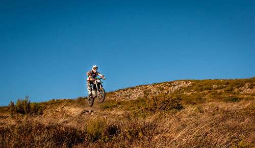 Man riding bicycle on mountain against clear blue sky