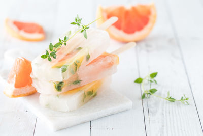 A small stack of grapefruit thyme popsicles on a white wood slate table.