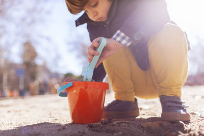 Low angle view of boy playing with sand pail and shovel while crouching at beach