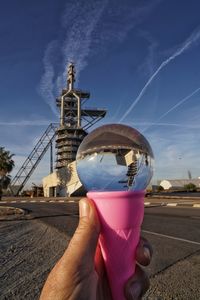 Cropped hand of person holding crystal ball against sky