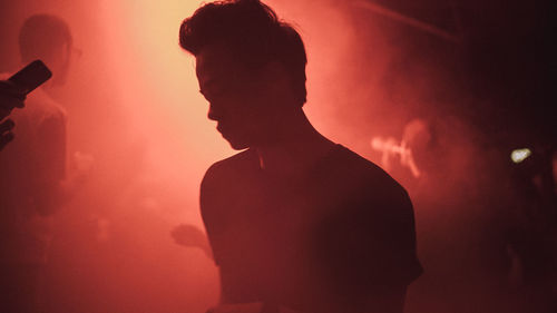 Silhouette man with arms raised standing at music concert