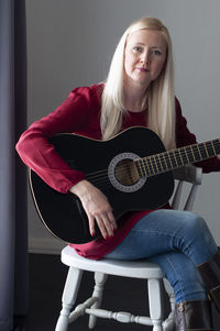 Beautiful young blonde woman in a red dress with a black guitar, favorite hobby