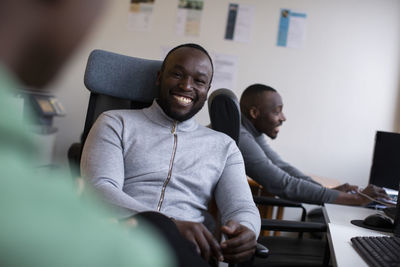 Portrait of cheerful businessman sitting on chair with coworkers in office