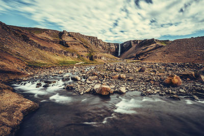 Surface level of water flowing through rocks against sky