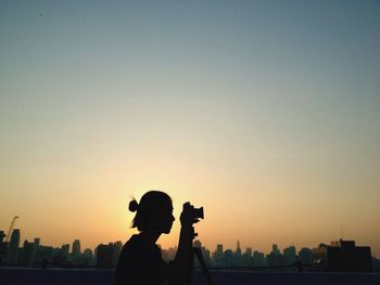 Silhouette people photographing cityscape against clear sky during sunset