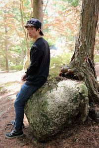 Side view of young man sitting on tree trunk in forest