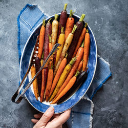 Top down view of a hand holding a serving dish of roasted rainbow carrots.