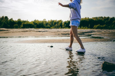 Low section of woman balancing on rocks at beach against sky