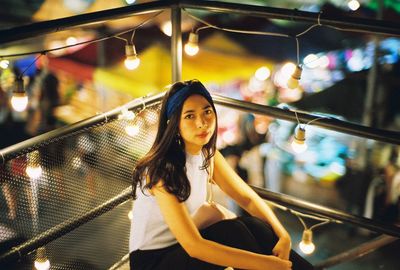 Portrait of woman standing against illuminated wall at night