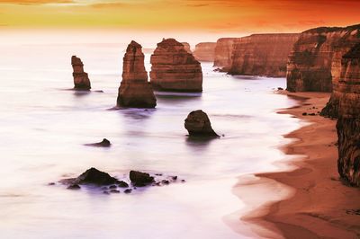 Rocks in sea against sky during sunset